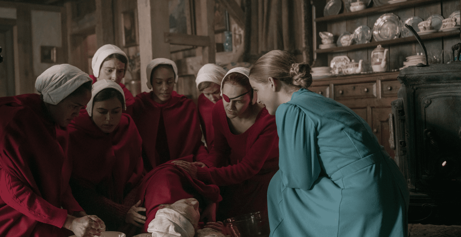 A woman lies on the floor while other women tend to her.