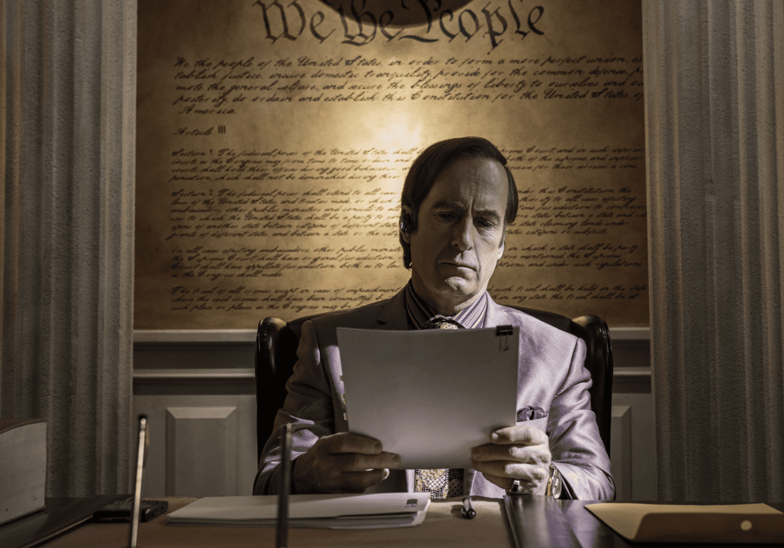 A man sitting at his desk with the text of the U.S. Constitution framed behind him 