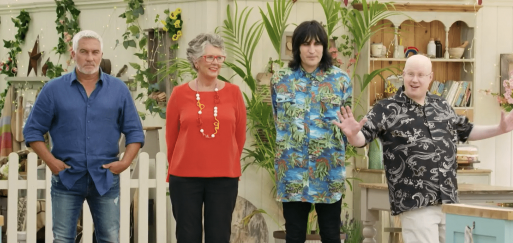 The hosts of The Great British Baking Show standing in a line, wearing an array of expressions and colors