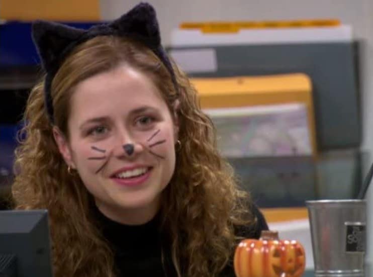 Pam Beesly from the show The Office behind her desk dressed as a black cat for Halloween