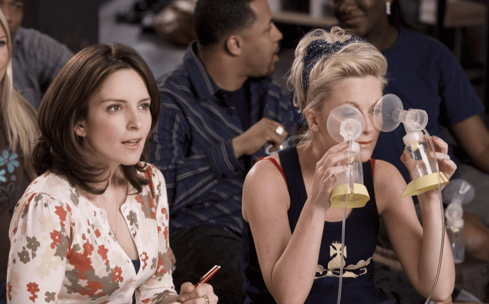 Tiny Fey intently listening to someone out of shot talk while Amy Poehler kneels next to her holding a set of suction cups to her eyes in this image from Broadway Video.
