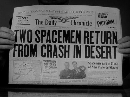 Person holding up a newspaper with the headline Two Spacemen Return From Crash in Desert