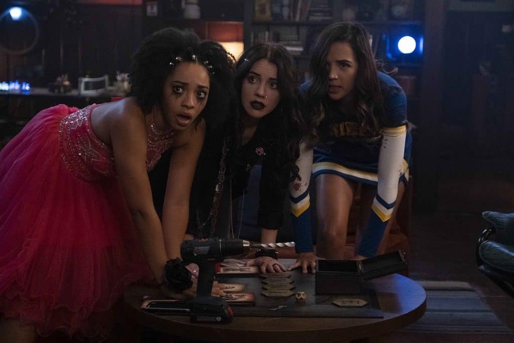 Three girls lean over a coffee table with a board game splayed out in this image from Blumhouse Television. 