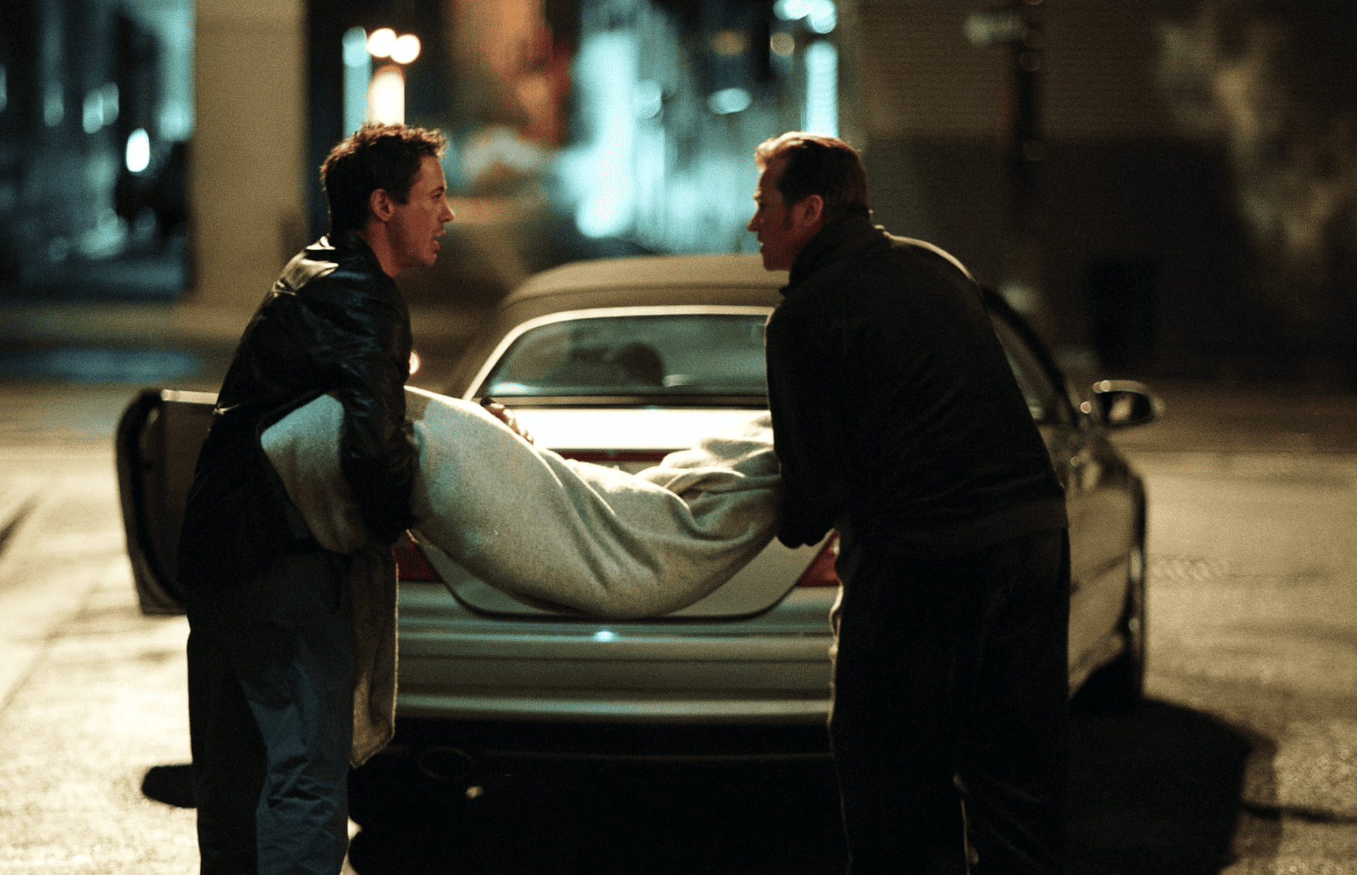 Two men argue as they carry a body wrapped in fabric towards a car in this image from Warner Bros.