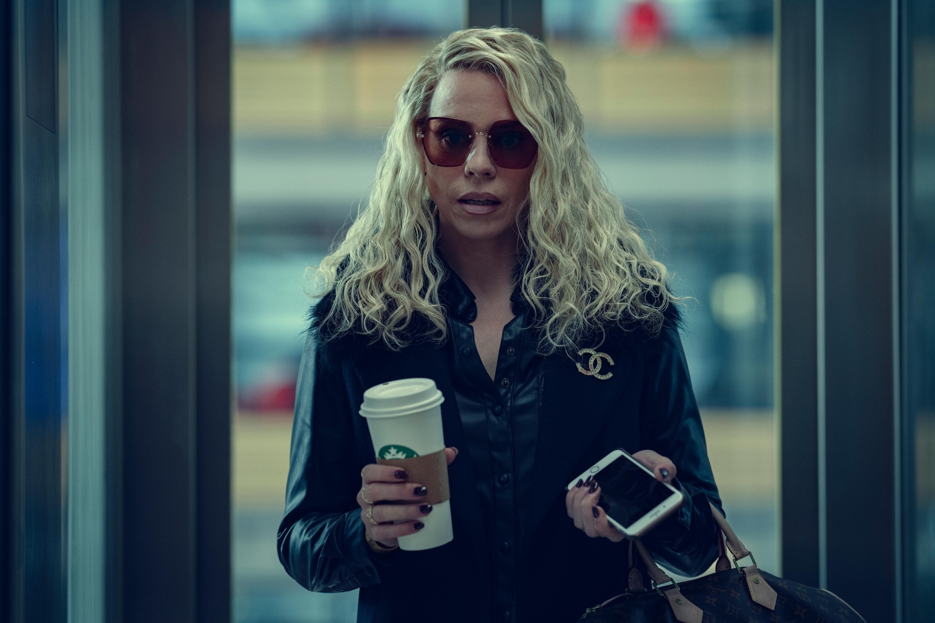 A woman holding Starbucks and a cell phone in this image from The Lighthouse.