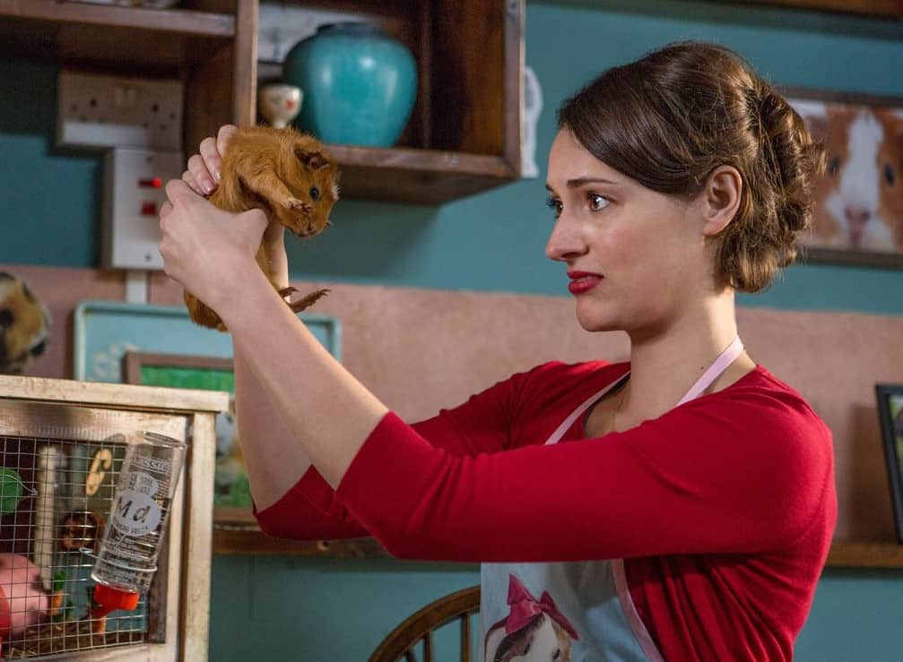 Fleabag holding a guinea pig while wearing a guinea pig apron