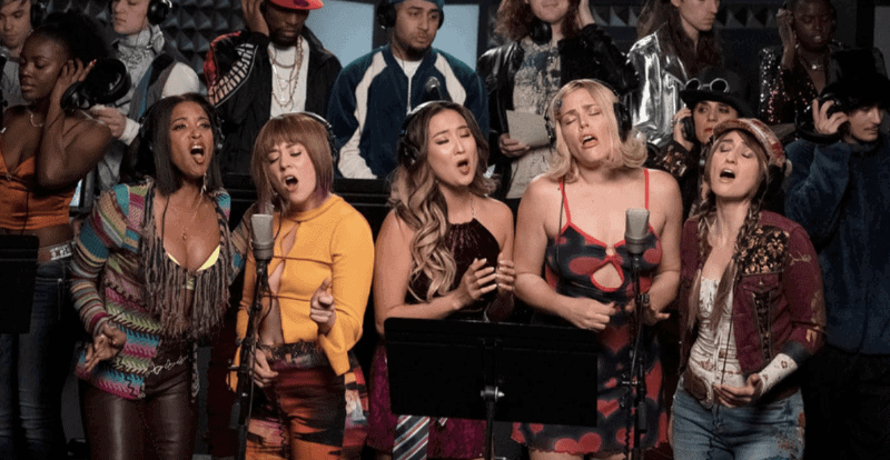 A group of five women sings emotionally into two microphones.