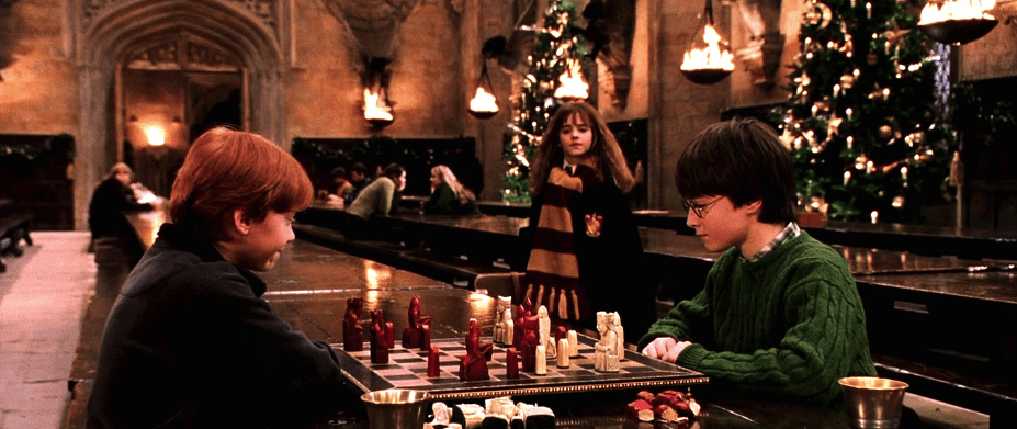 Two boys play wizard chess in the Great Hall as their friend watches in this image from Warner Bros.