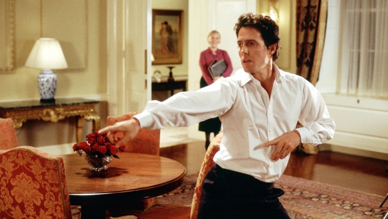 A man in a white button-up shirt dances after hours with the housekeeper looking on in this image from Universal Pictures. 