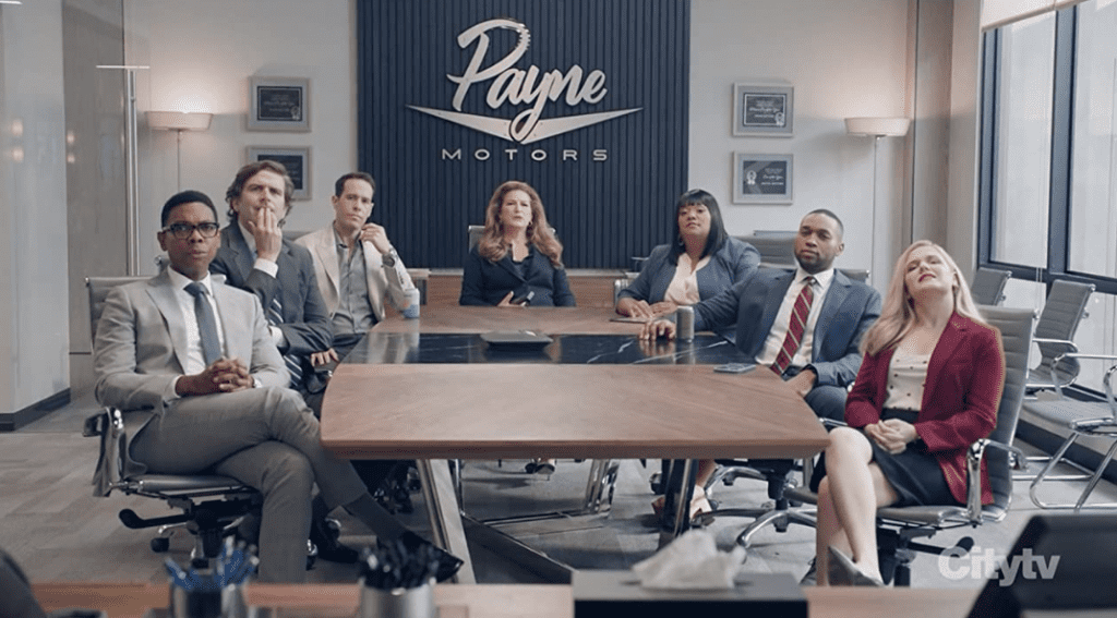 Cast of “American Auto” sitting around a conference table at Payne Motors