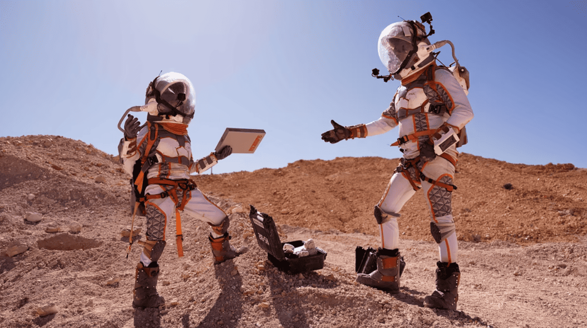 Two astronauts stand alongside a box of supplies on Mars in this image from Eureka Productions.