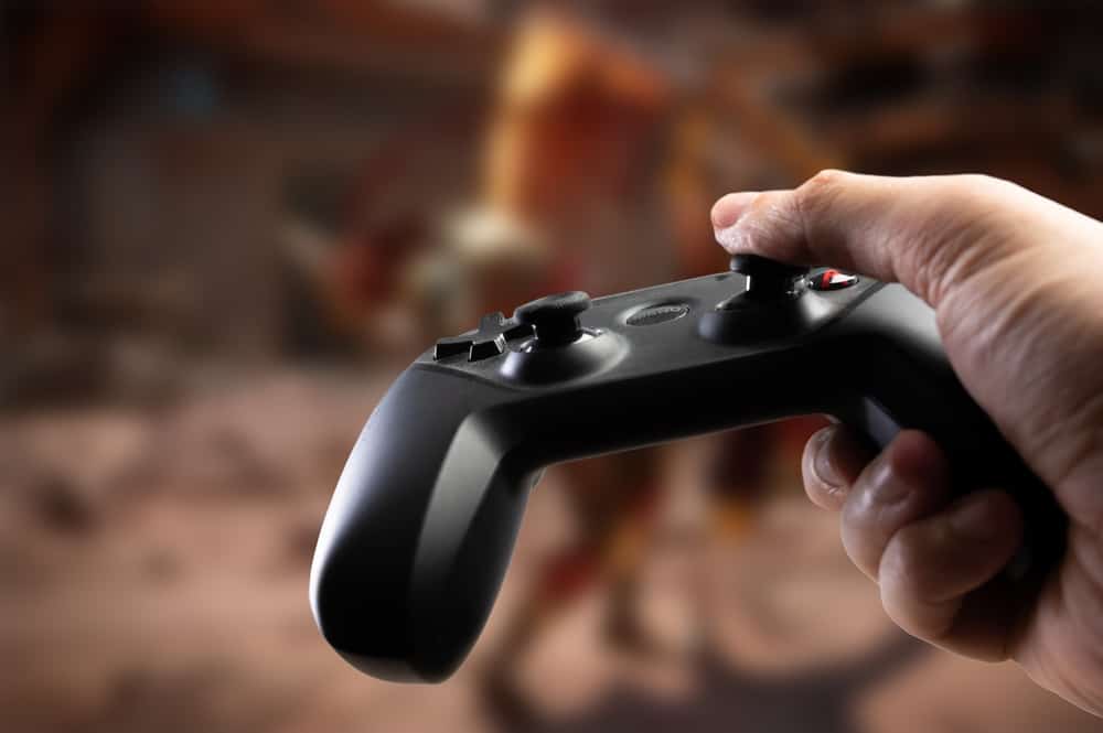 A person holding a black game controller with a blurred background