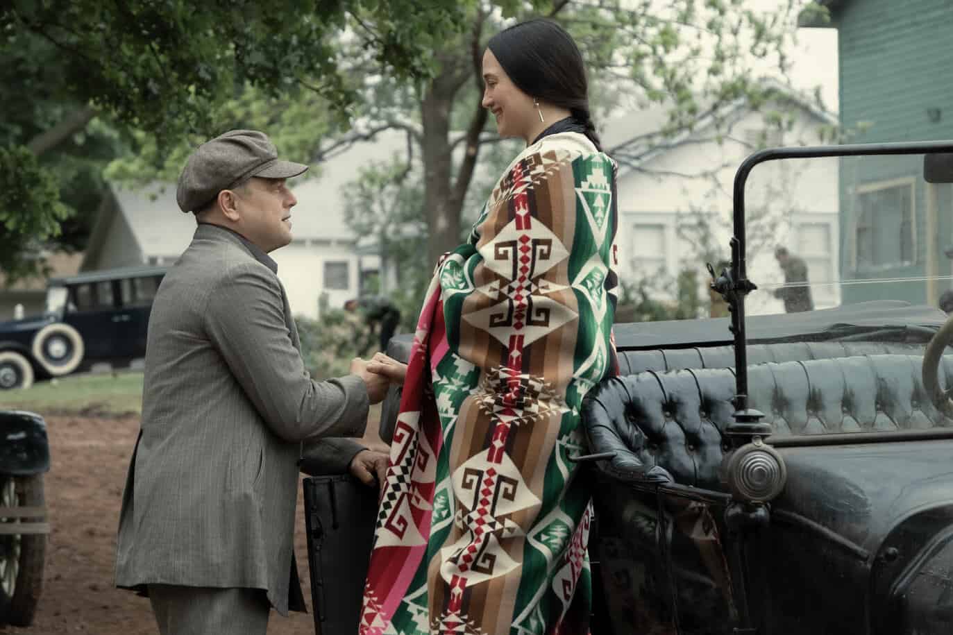 A man in a suit and cap helping a Native American woman out of a vintage car in this image from Apple Studios.