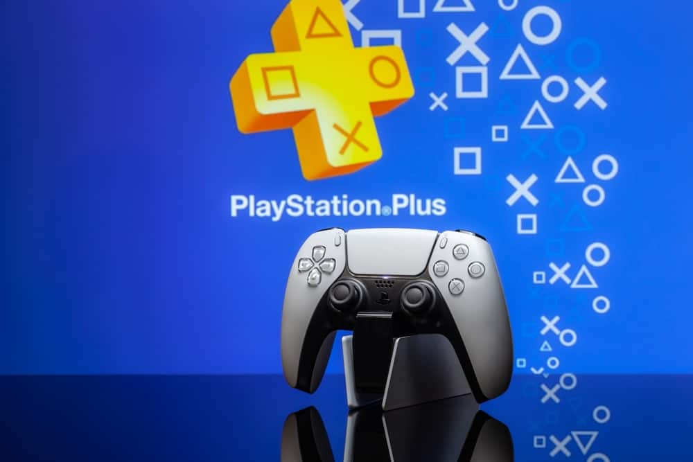 A docked PlayStation 5 controller with the PlayStation Plus logo in the background