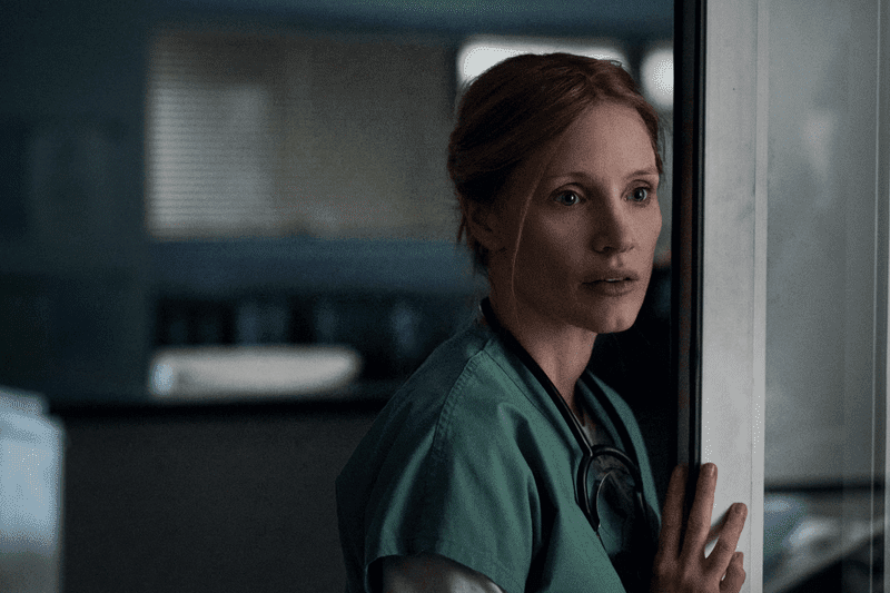 Amy in scrubs leaning on a doorway in the hospital