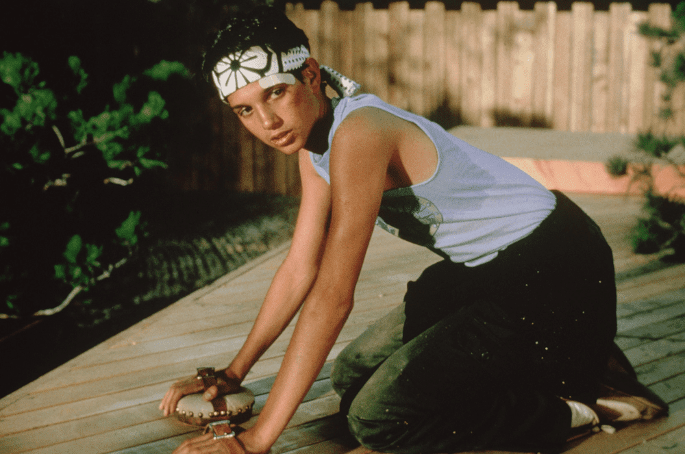 Daniel scrubbing a deck in a sweatband and muscle shirt