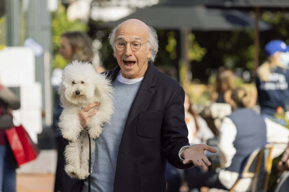 Larry David looking excited holding a fluffy white dog in this image from HBO Entertainment.
