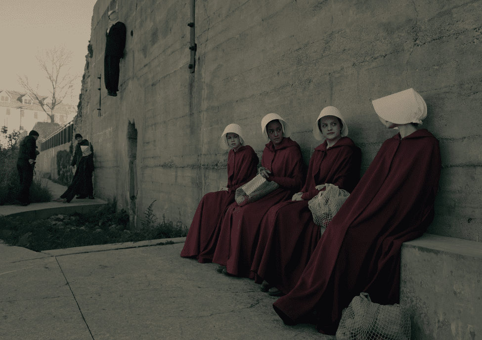  A group of handmaids sitting against a cement wall