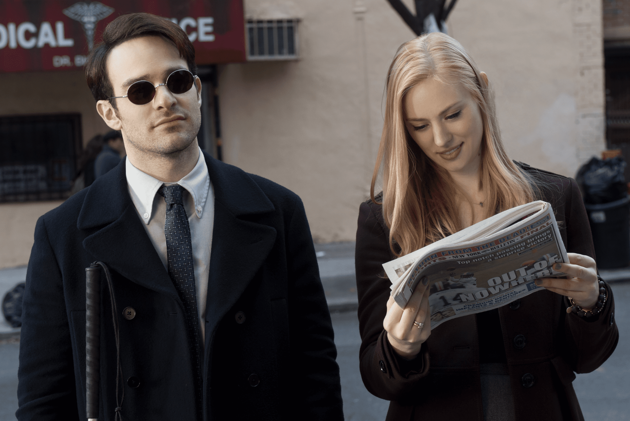 A man and woman walk together while she looks at a newspaper in this image from ABC Signature.