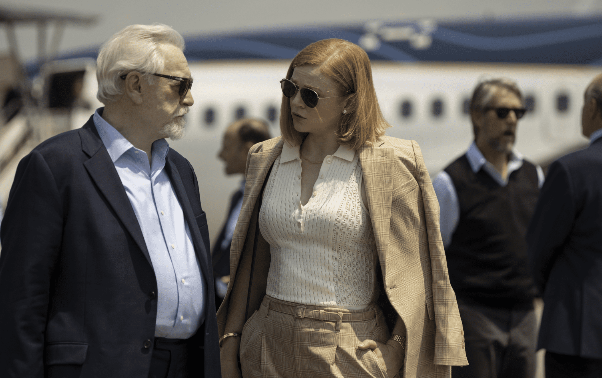 Two of the main characters of “Succession,” dressed in business casual clothes, confer closely outside on a sunny day