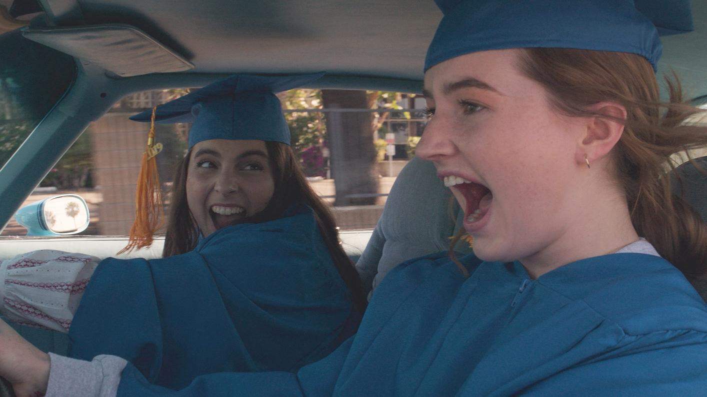 Molly and Amy driving fast in their graduation caps