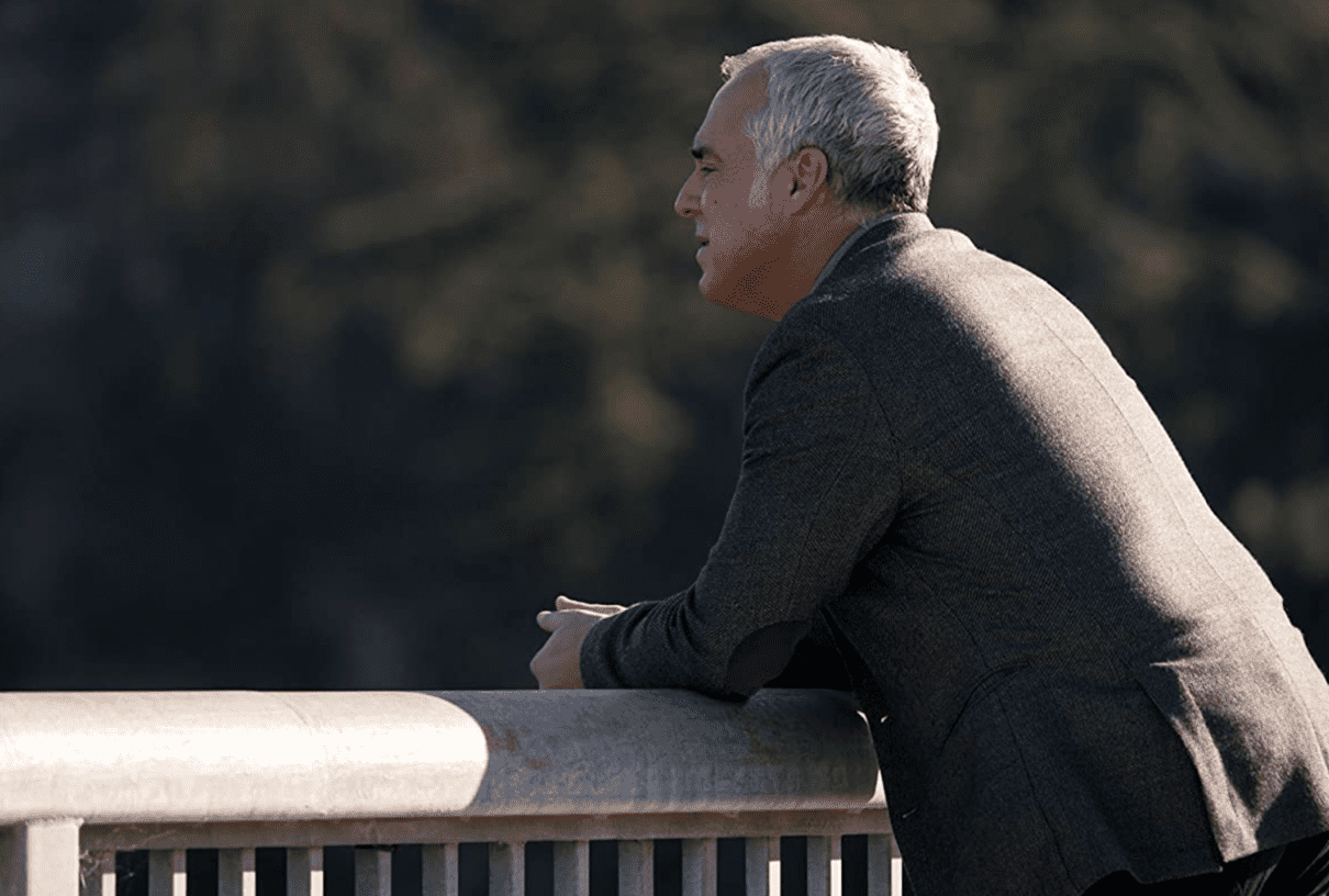 A man leans on a bridge and stares into the distance showing signs of exhaustion.