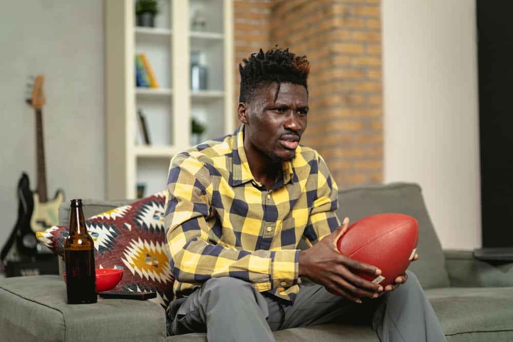 A man holding a football while sitting on a couch and frowning