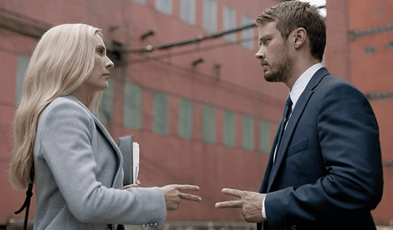 Detective Albans (Aliette Opheim) and John Tavner (Michael Dorman) stand outside what resemble government offices and communicate with secret signs.