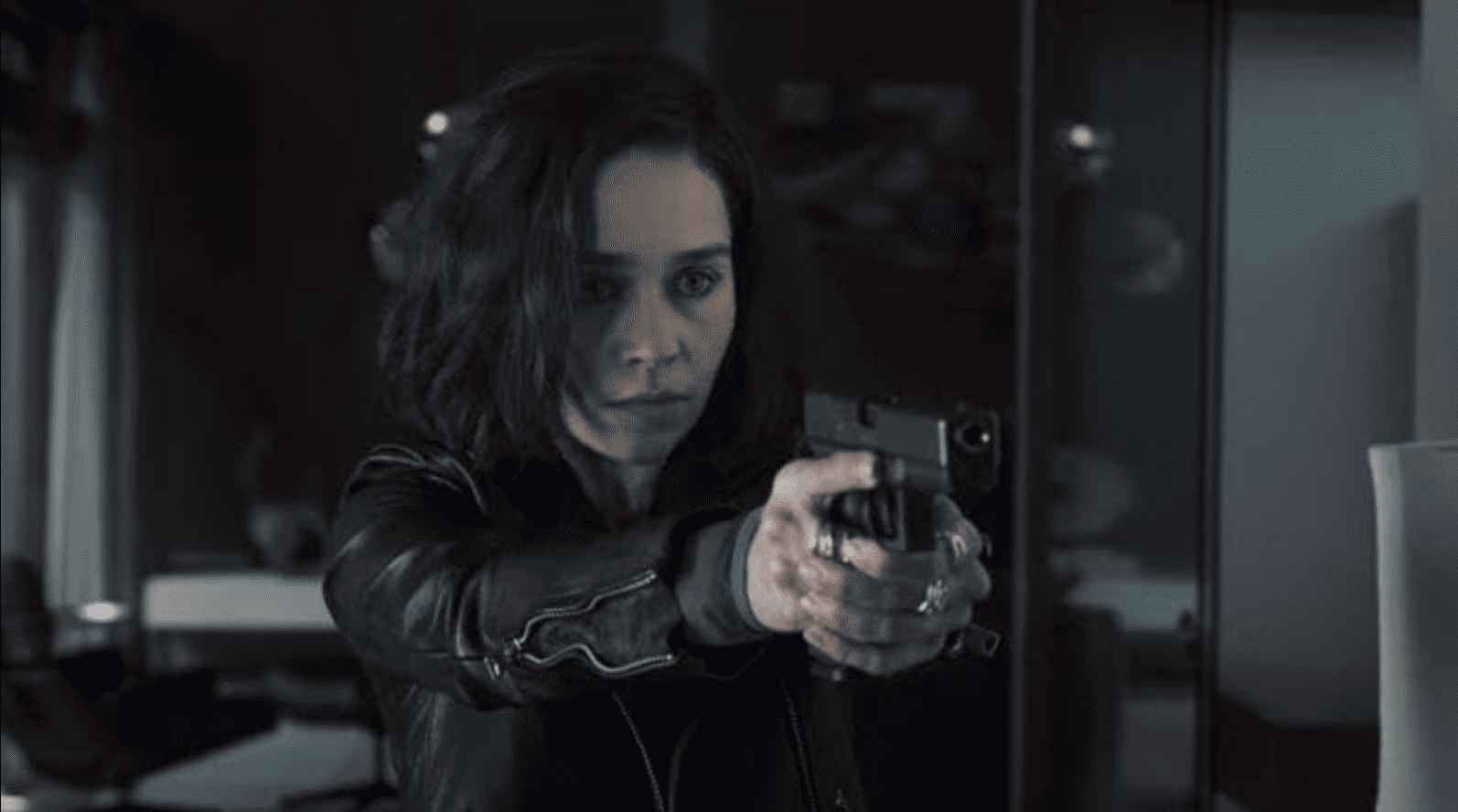 A woman in a leather jacket points a gun at someone off-screen in this image from Marvel Studios.