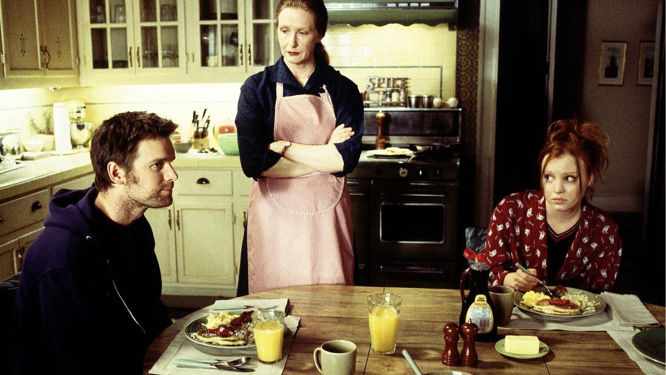 Ruth standing over her children at the breakfast table with arms crossed