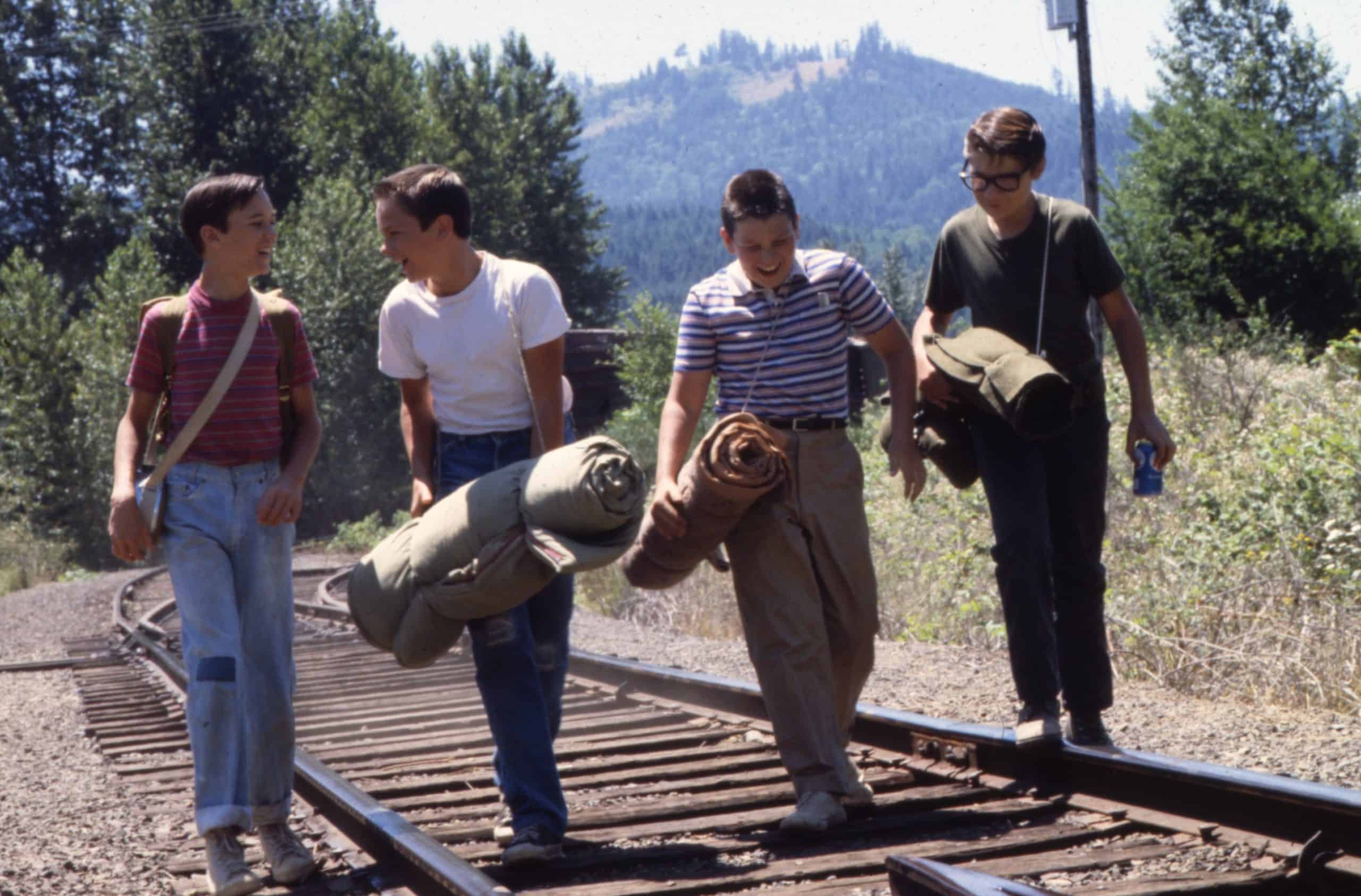 Four friends walking on a railroad track carrying bedrolls