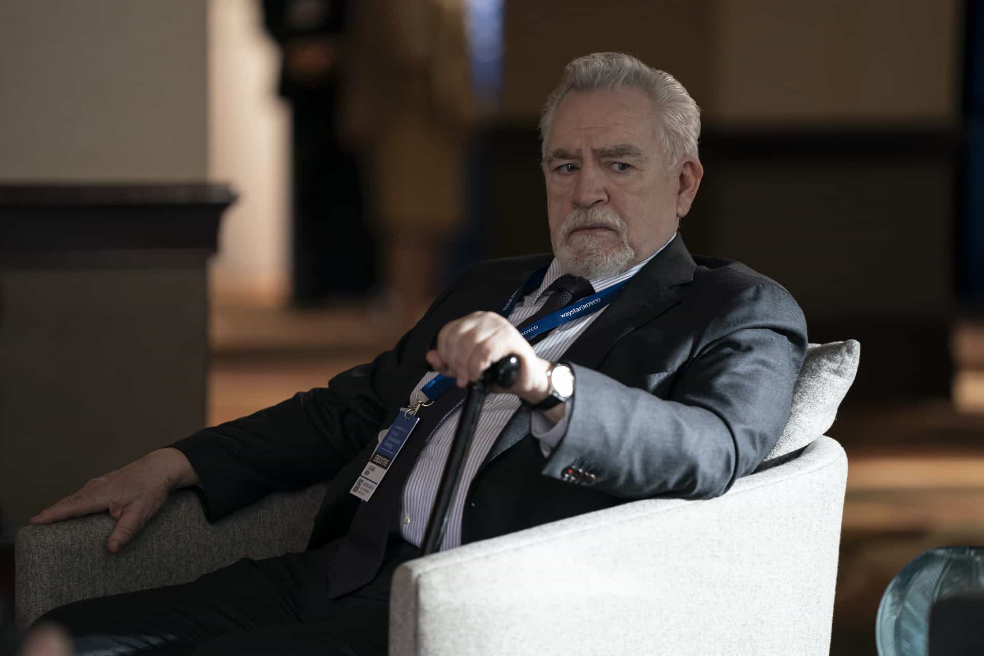 Logan in a suit and name badge looking worried in an armchair