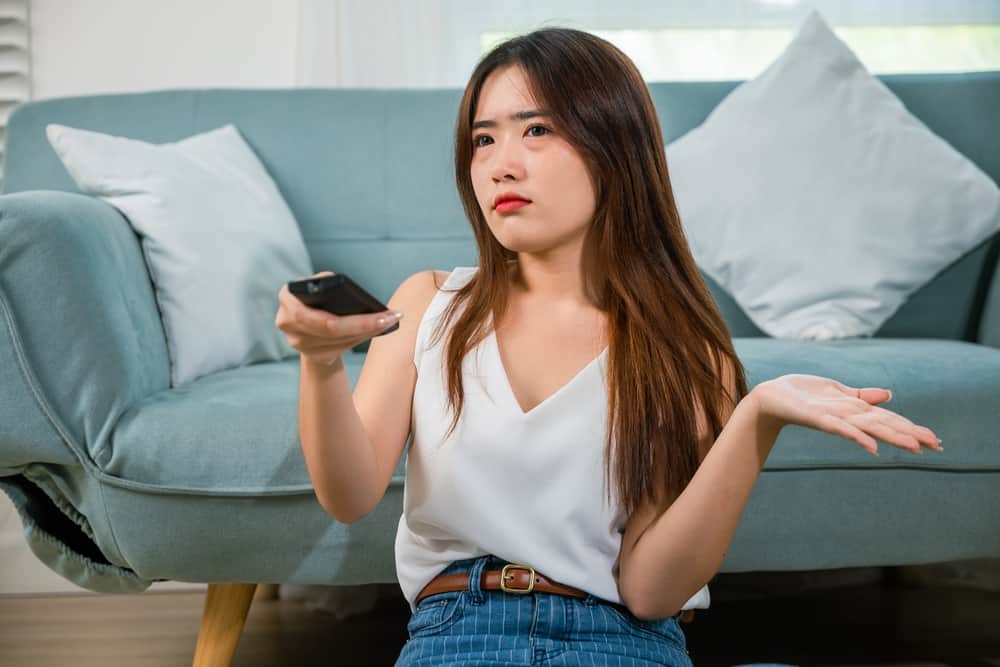 A young woman frowning as she holds a TV remote