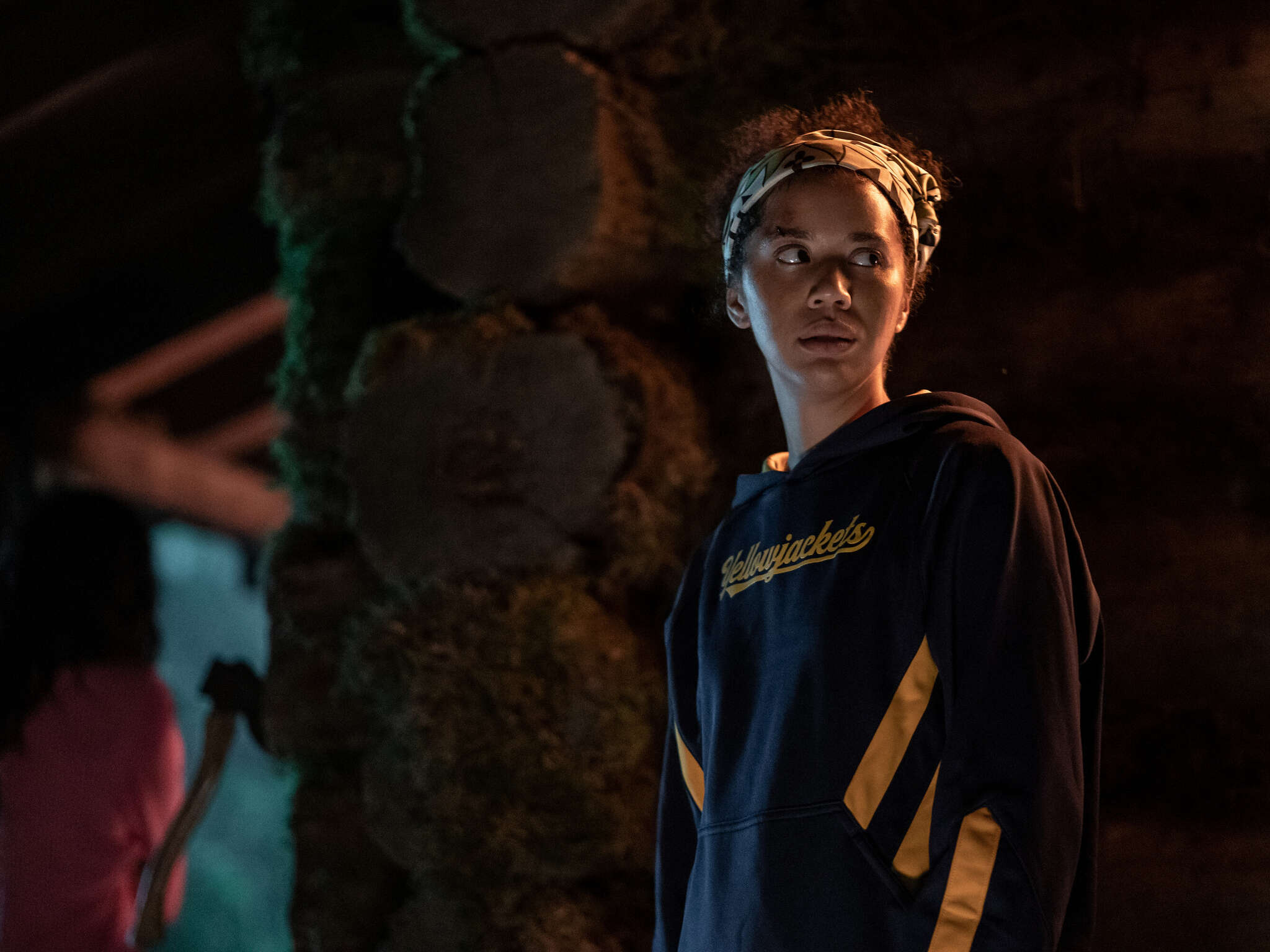 Taissa in a Yellowjackets team hoodie looking worried in the forest