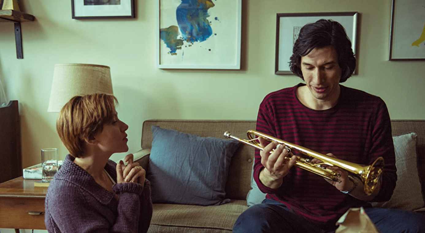 A woman sitting on the floor and a man on the couch with a trumpet in this image from Netflix