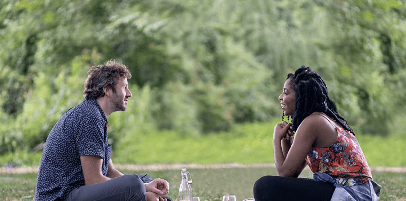 A man and a woman sitting across each other by the lake in this image from Netflix