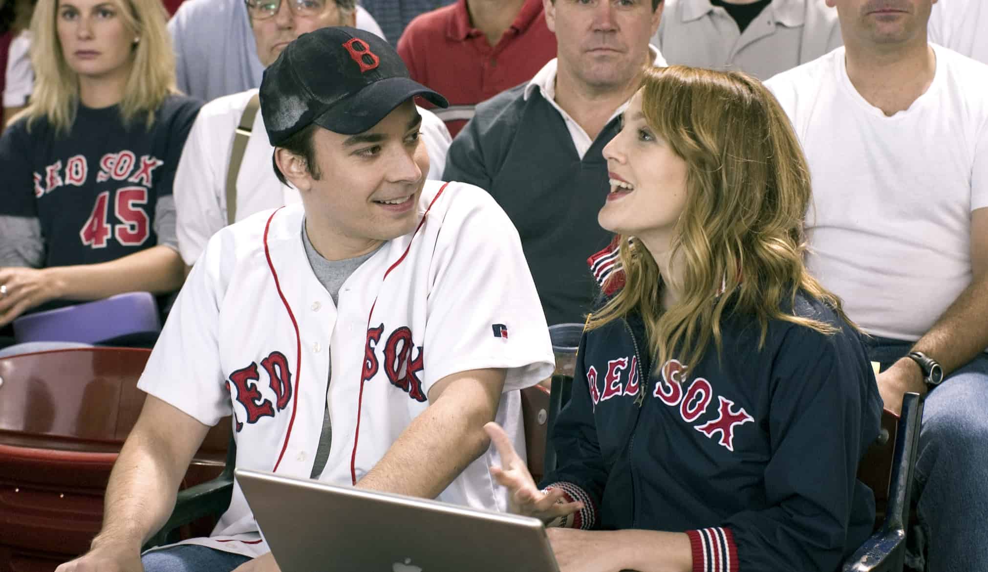 A man wearing a Red Sox jersey and cap sitting next to a woman wearing a Red Sox jacket in this image from Amazon Prime Video