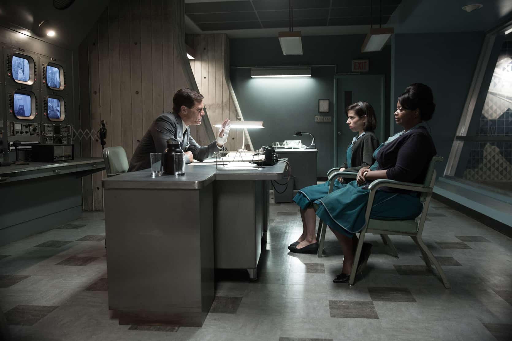 A man talks to two women in a retro-future office in this photo from Searchlight Pictures.
