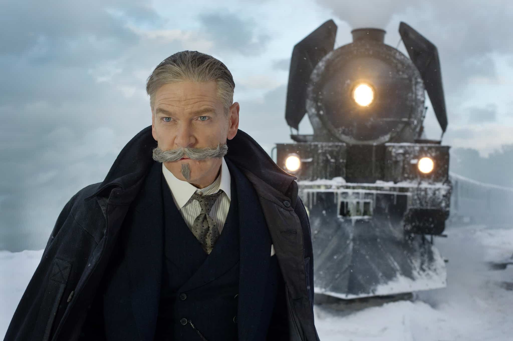 A man with an impressive mustache and beard stands in front of a train