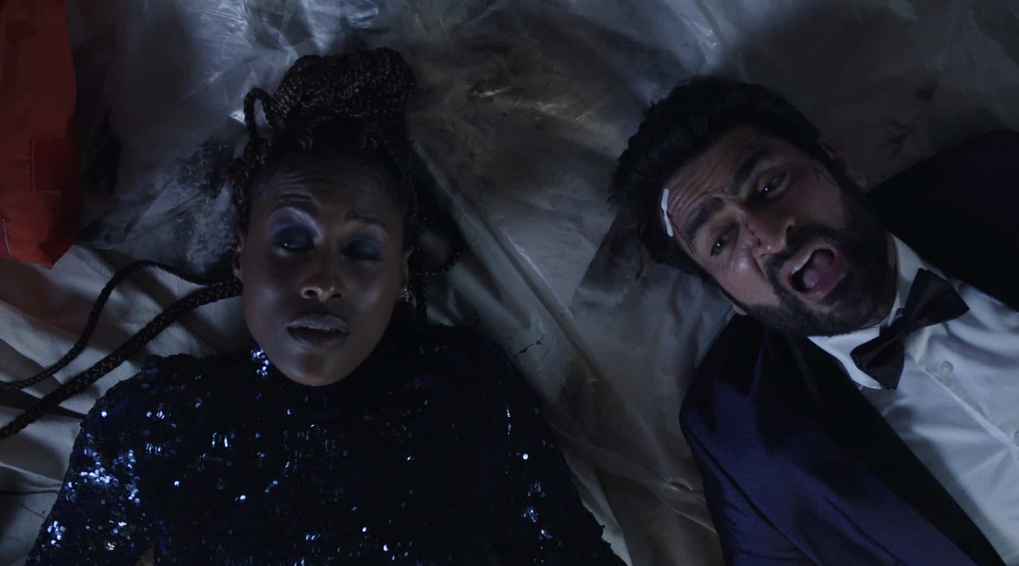 A Black woman with braids in a bun wearing a black sequined turtleneck and a beaten-up man in a tux is next to her in this image from Netflix.