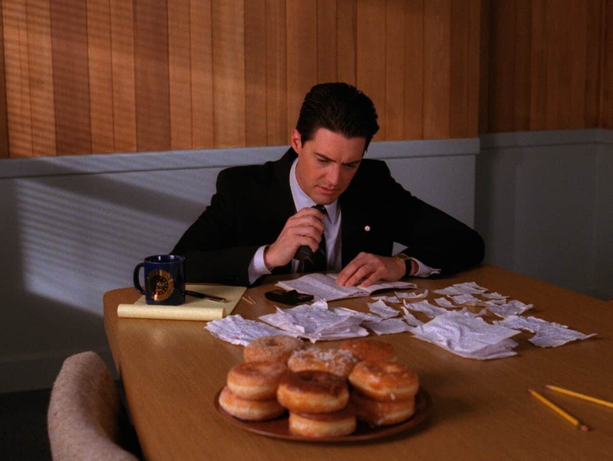 A man sits at a table with shredded paper and a plate of donuts