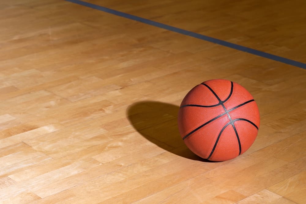 Basketball on polished hardwood court with lighting in this image from Shutterstock 