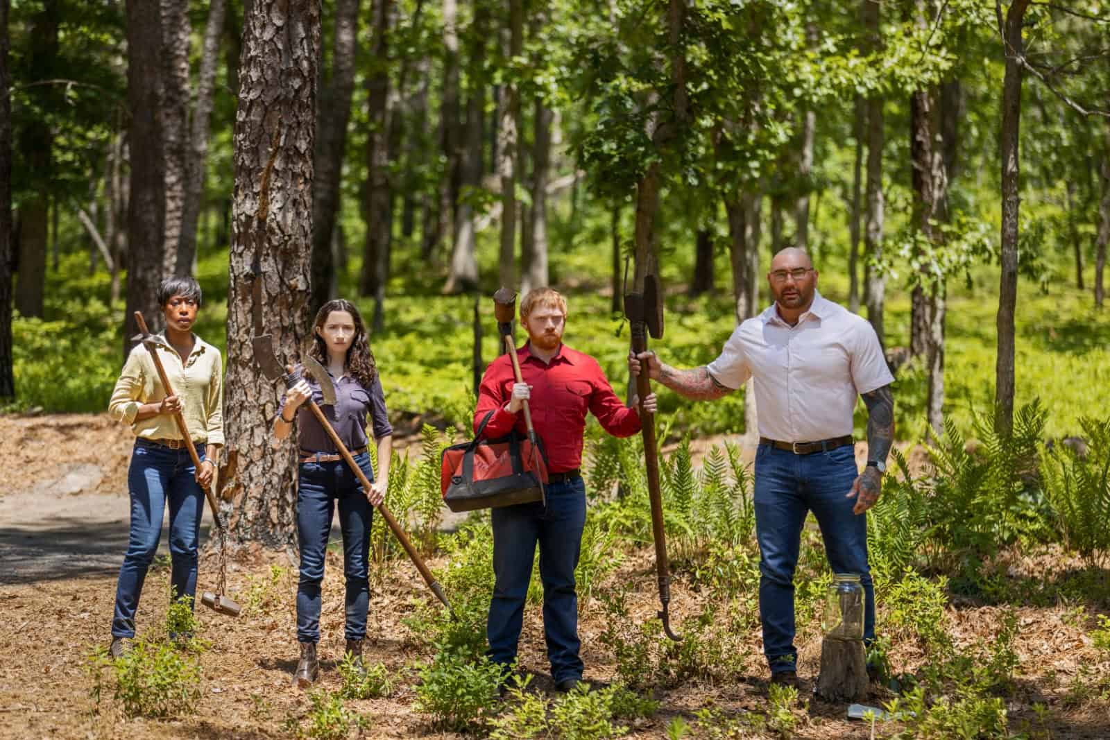 Four people holding pickaxes in the woods in this image from Peacock