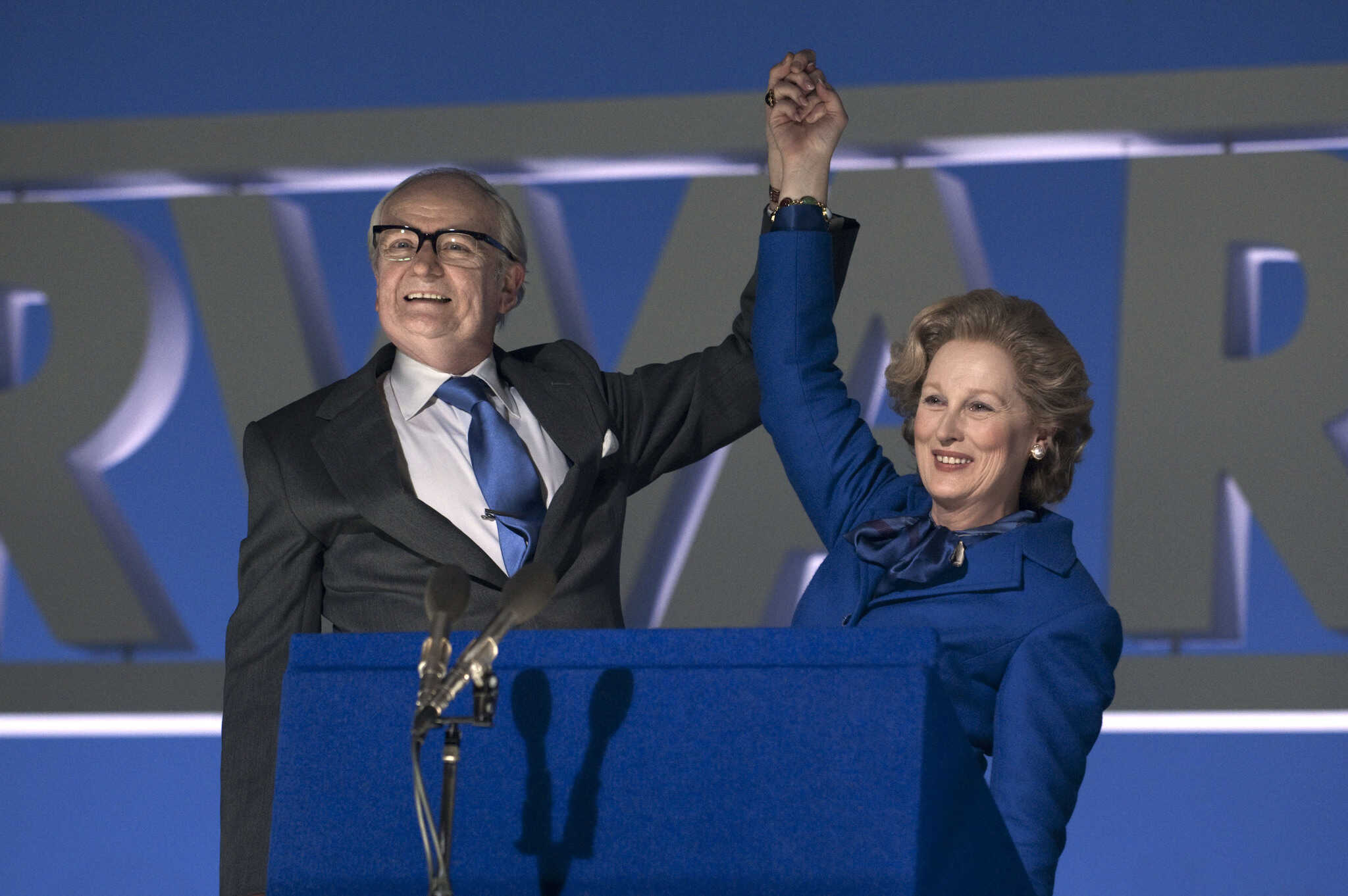 A pair of politicians raise their clasped hands on stage in this photo from DJ Films.
