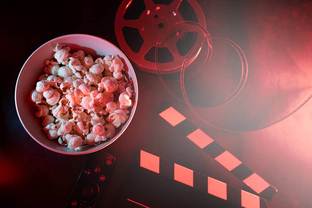 A bowl of popcorn, a film reel, a remote, and a director’s slate in this image from Shutterstock