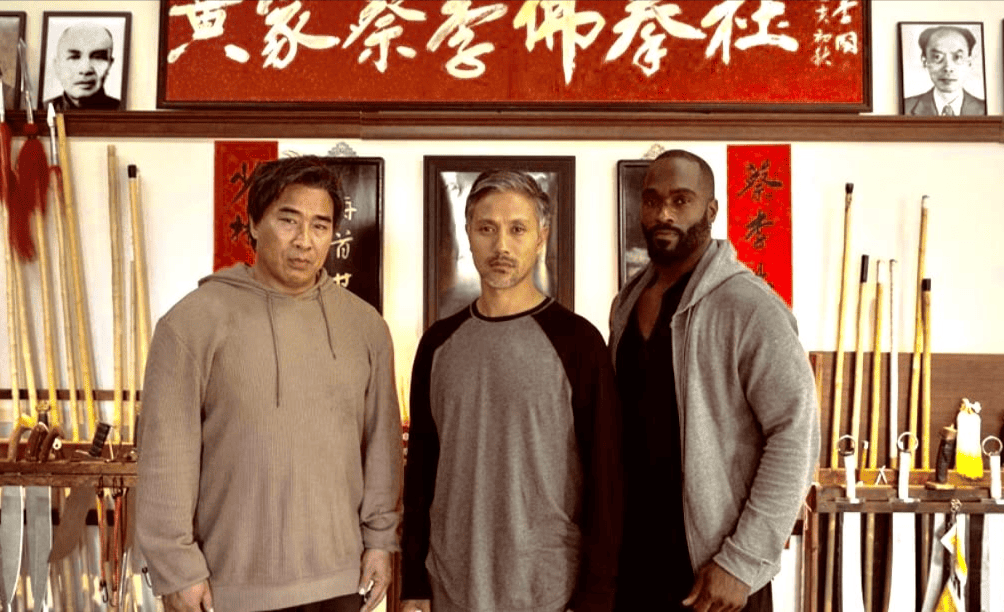 Three men standing together in front of martial arts weapons in this image from Beimo Films