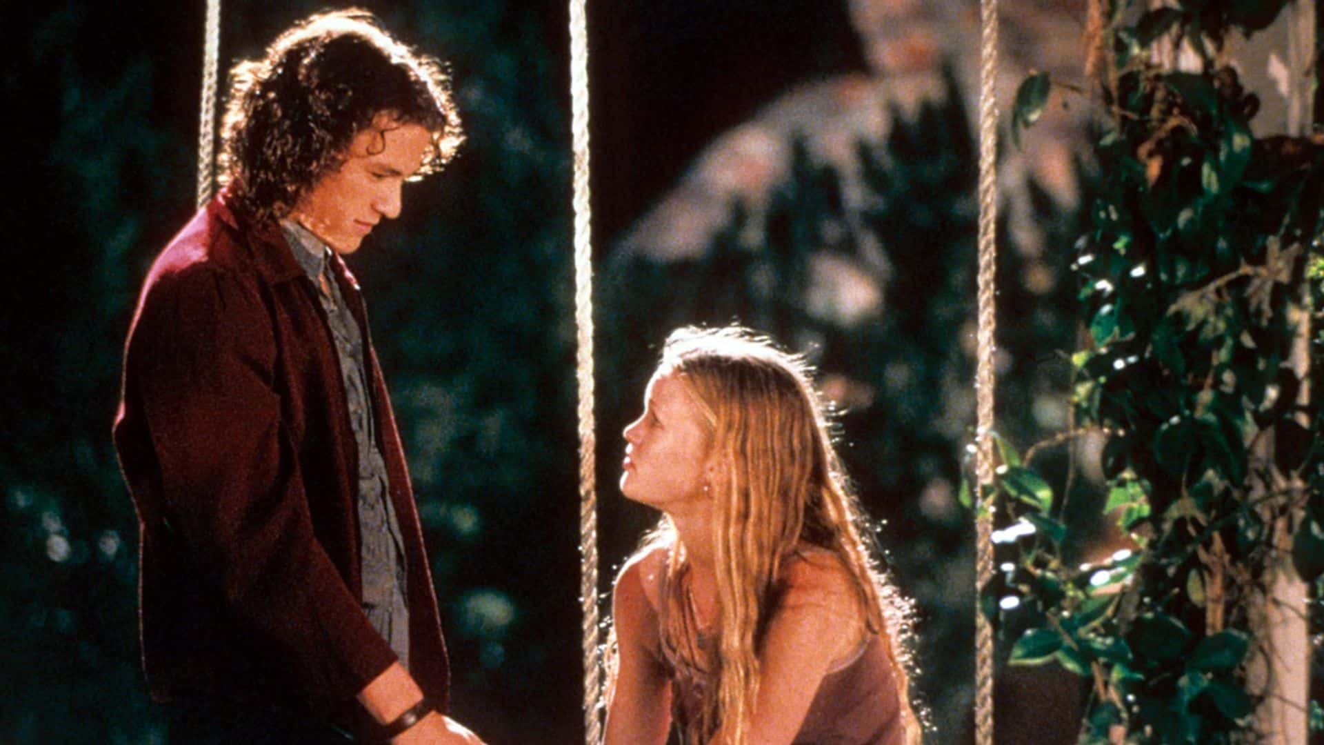 Heath Ledger stands next to Julia Stiles sitting on a swing in this image from Touchstone Pictures.