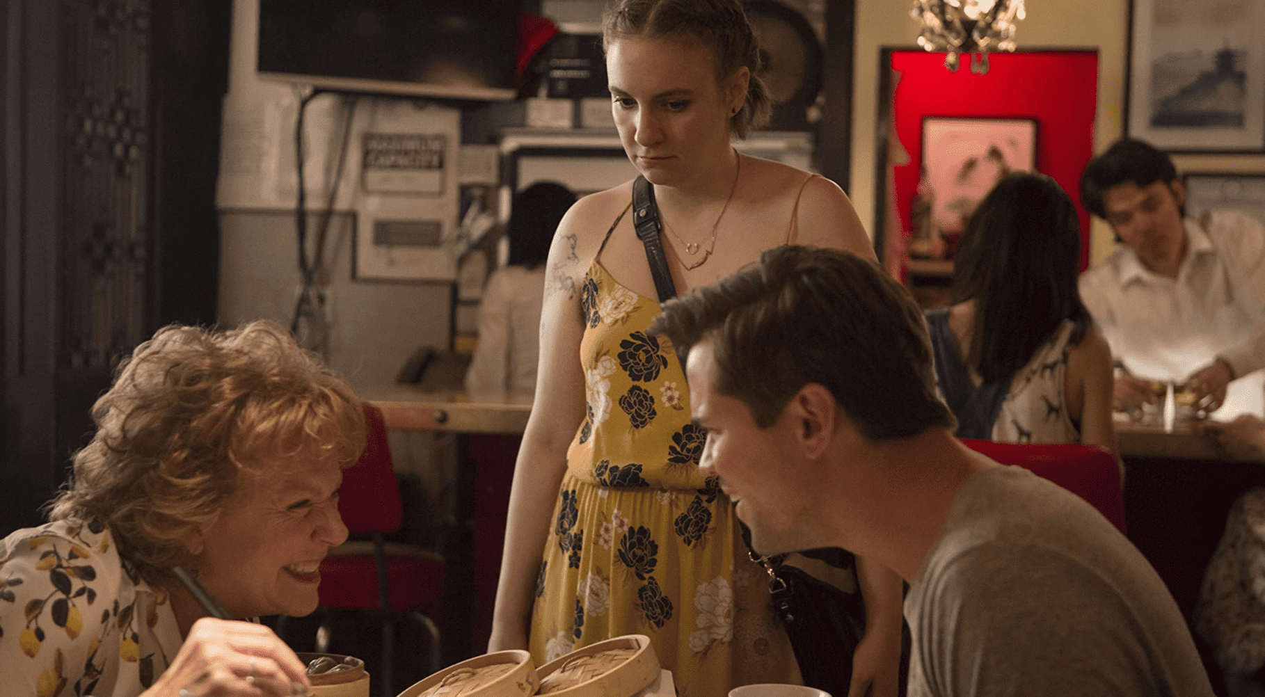 Elijah eating and laughing with Hannah’s mom while Hannah looks unamused in this image from Apatow Productions