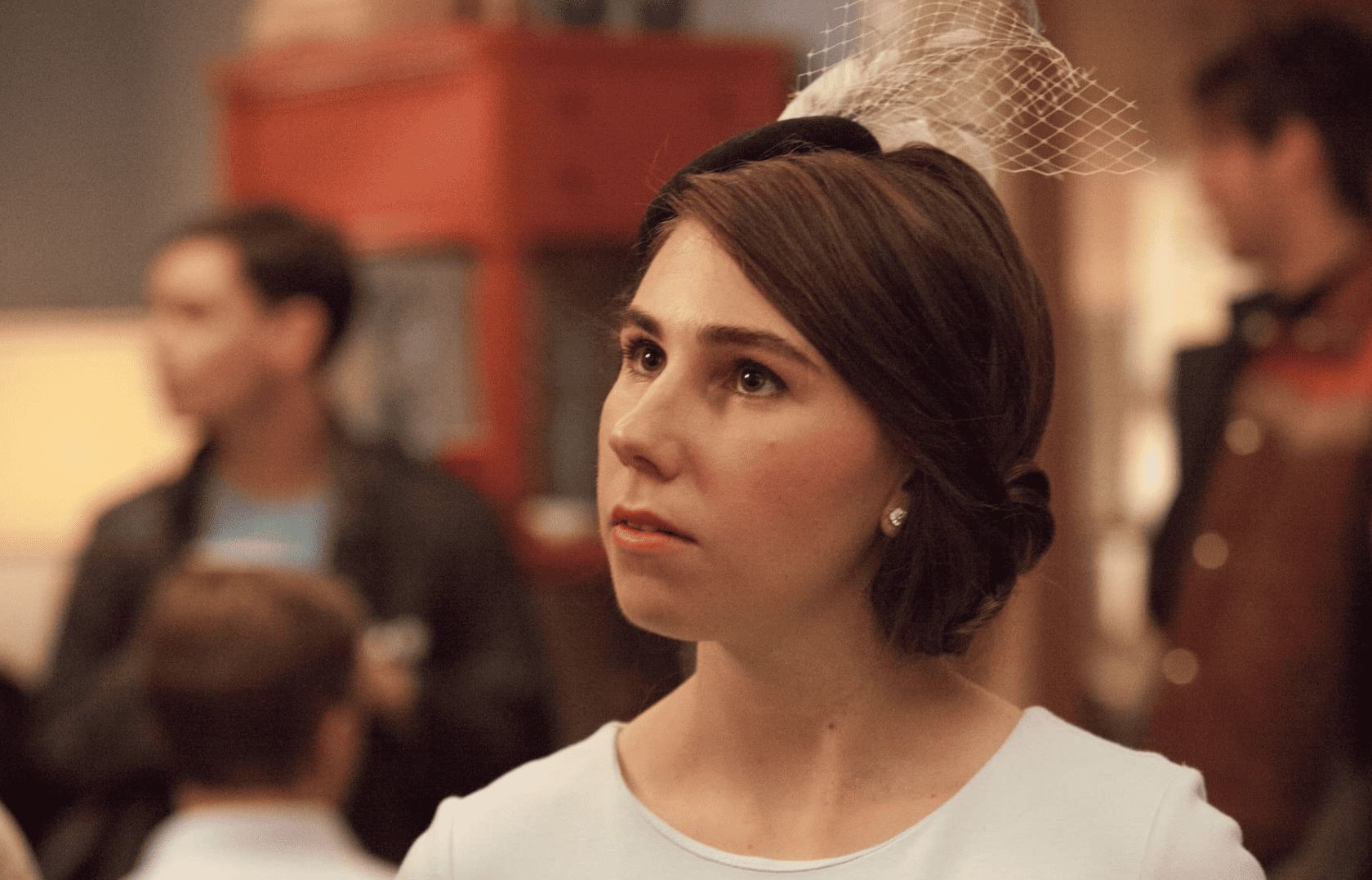 Shoshana is wearing a fascinator and soft-blue dress in this image from Apatow Productions.