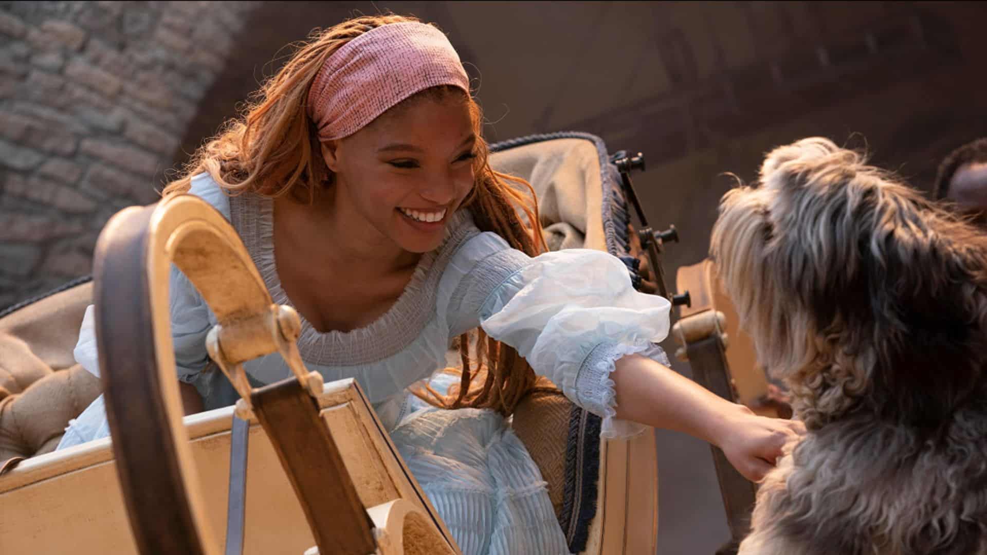 Halle Bailey sitting in a carriage and petting a dog in this image from Walt Disney Pictures.